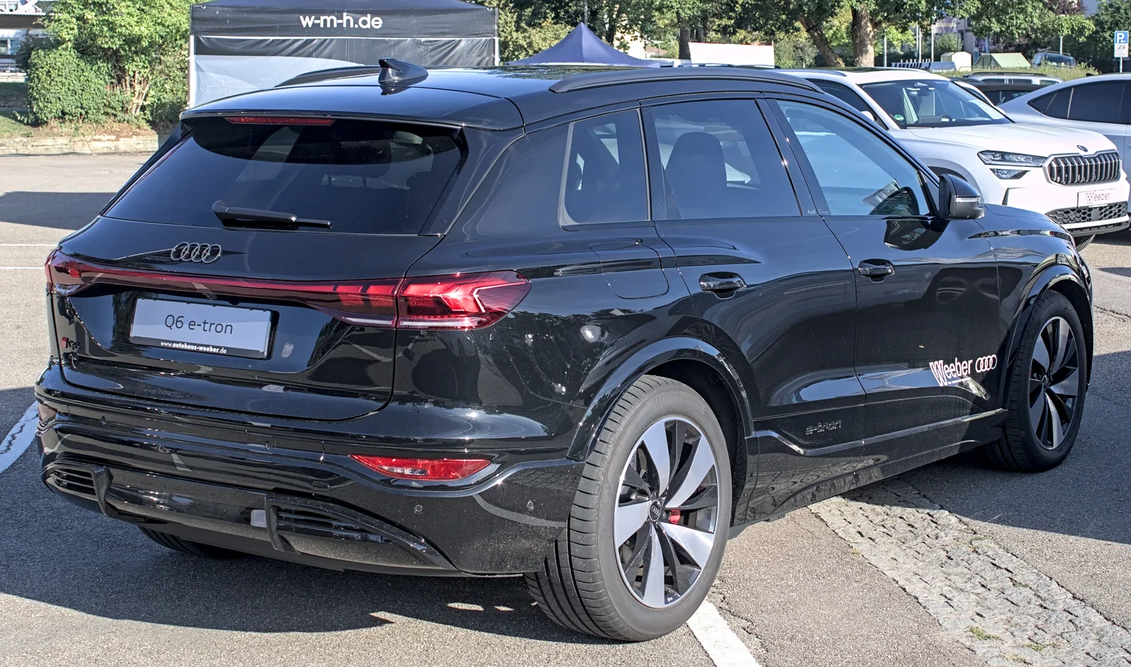 Audi Q6 e-tron 2026 vue trois quarts arrière sur un parking, plaque immatriculée Q6 e-tron