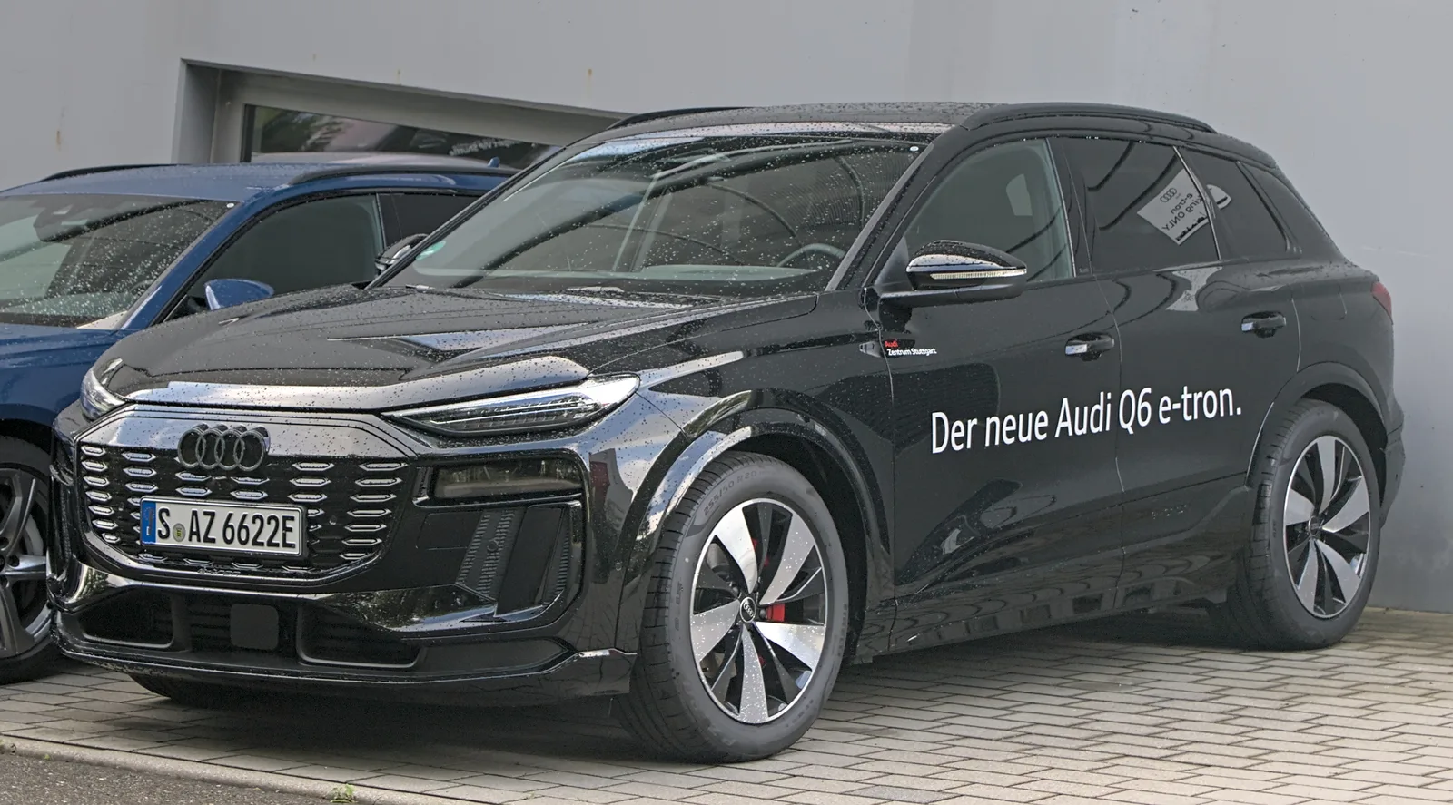 Audi Q6 e-tron 2026 vue avant trois quarts, version noire garée devant un centre Audi