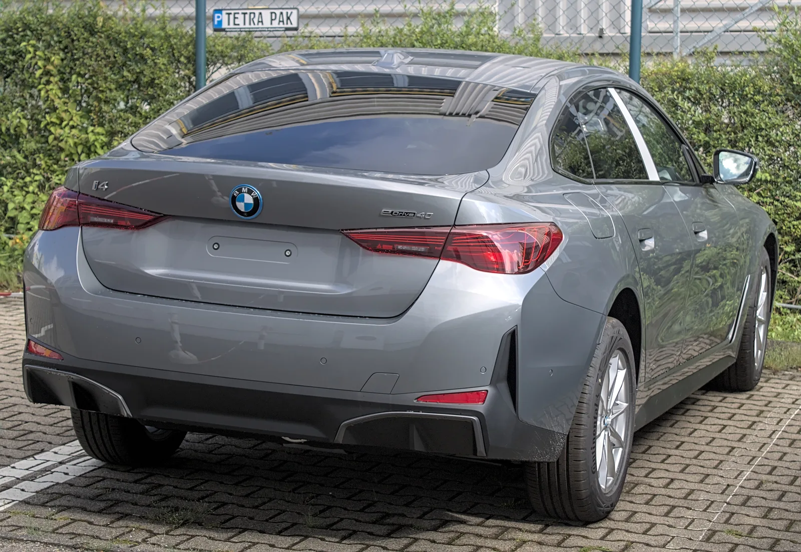 Vue arrière de la BMW i4 2026 grise en parking, badge BMW et feux de position allumés