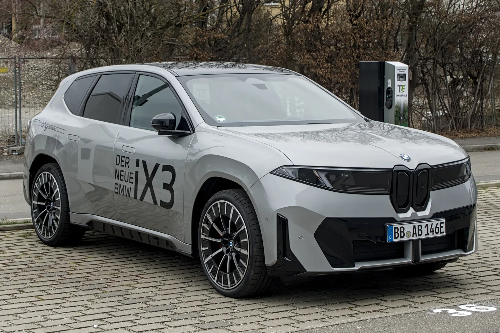 BMW iX3 Neue Klasse gris garé devant une borne de recharge, SUV électrique qui récupère 372 km en 10 minutes selon BMW