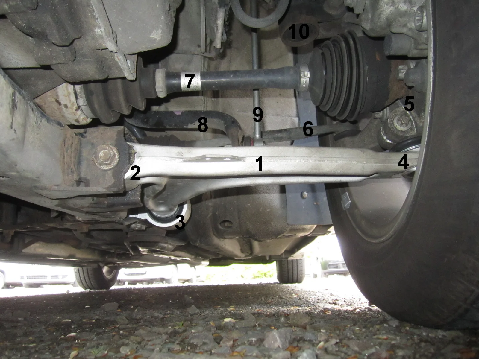 Dessous de caisse d'une voiture sur pont — composants de suspension et de transmission visibles avec bras de triangulation et demi-arbre