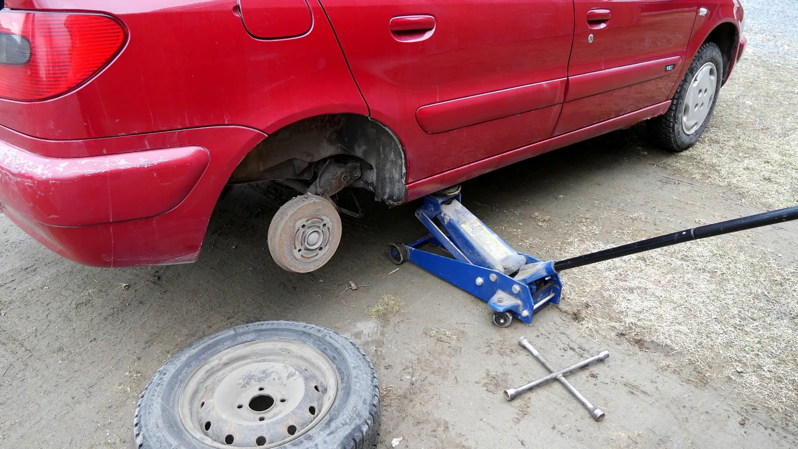 Voiture rouge sur cric hydraulique, pneu retiré, en cours de changement de roue