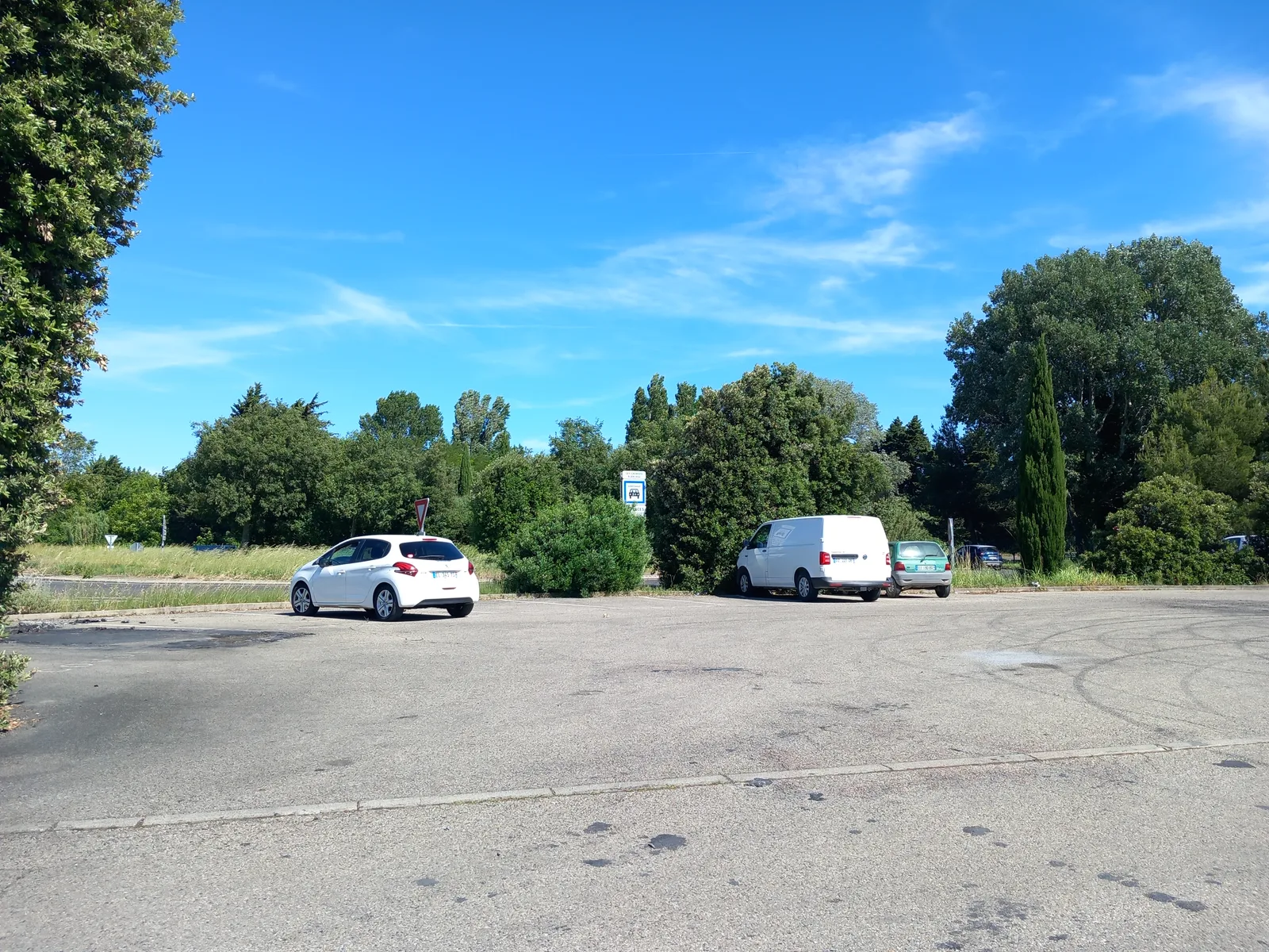 Voiture blanche garée sur un parking près d'une camionnette et d'un panneau de covoiturage