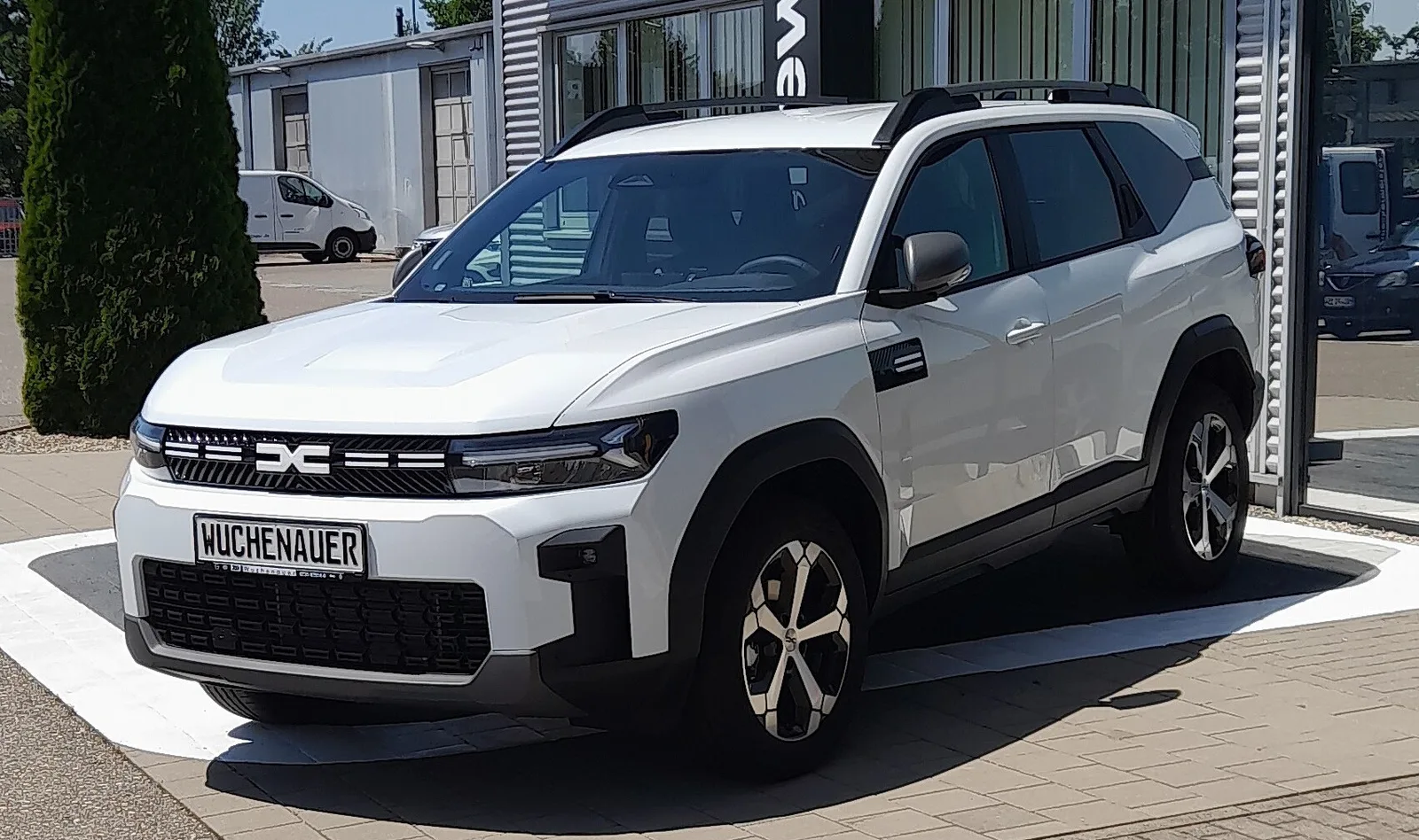 Dacia Bigster blanc vu de trois quarts avant devant une concession, SUV hybride familial noté 3 étoiles Euro NCAP mais 85 % en protection des enfants