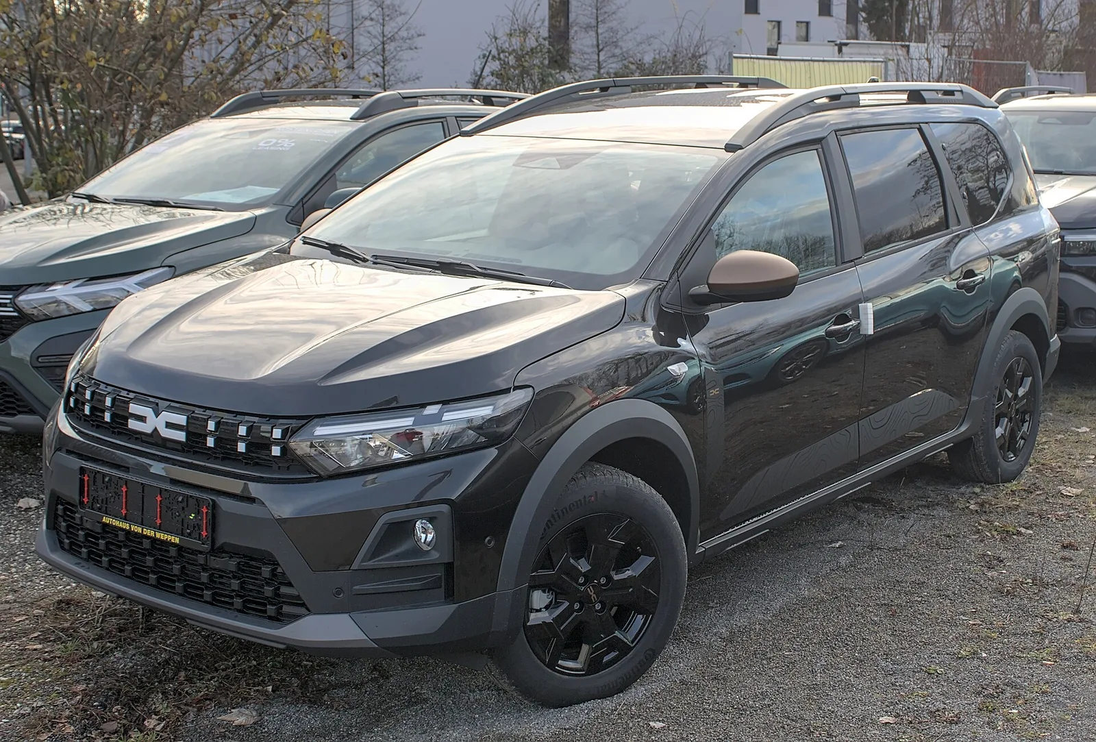 Dacia Jogger Hybrid noir vu de trois quarts avant sur un parking de concession, hybride familiale 7 places parmi les moins gourmandes