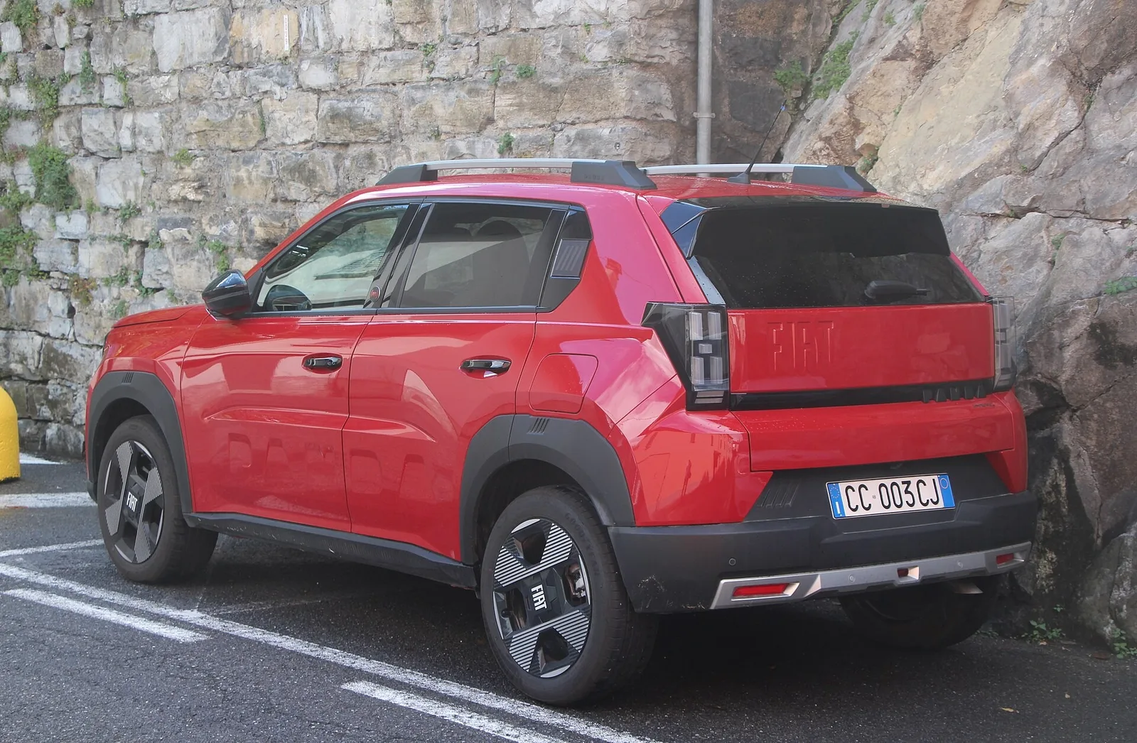 Fiat Grande Panda rouge vue de trois quarts arrière garée au bord d'un lac, citadine dont la finition Icône ajoute écran tactile et caméra de recul