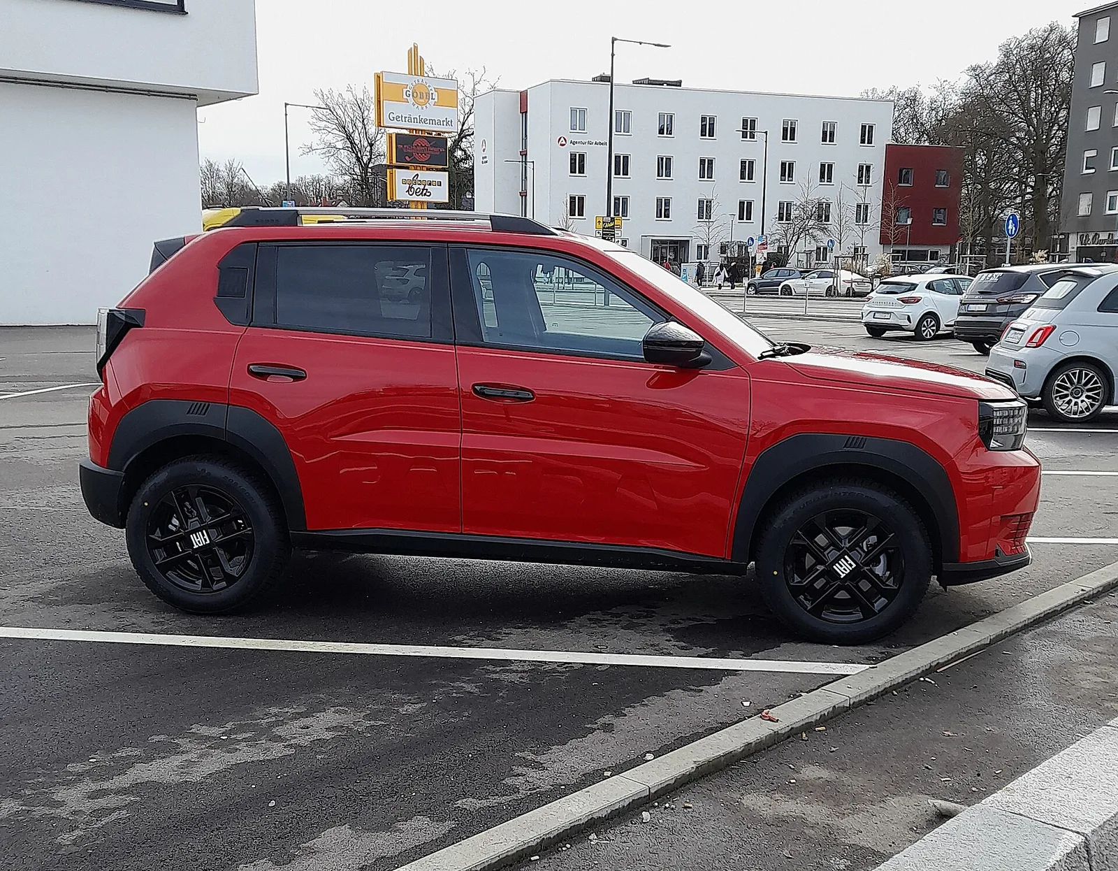 Fiat Grande Panda rouge vue de profil sur un parking, citadine à cinq places proposée en électrique avec 361 litres de coffre