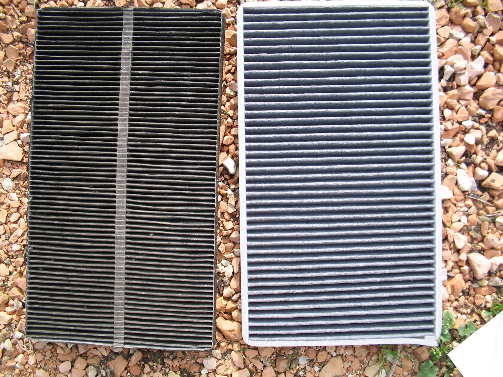 Comparaison filtre habitacle usagé noir et filtre neuf gris clair, posés côte à côte