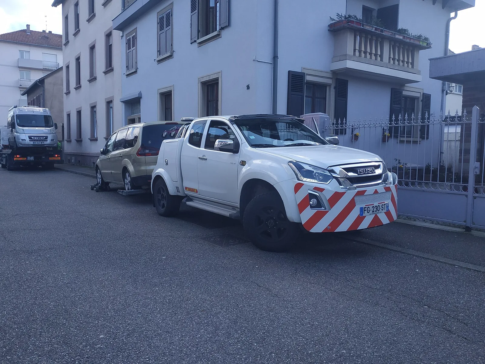 Dépanneuse d'une fourrière communautaire remorquant une voiture sur chariots dans une rue résidentielle