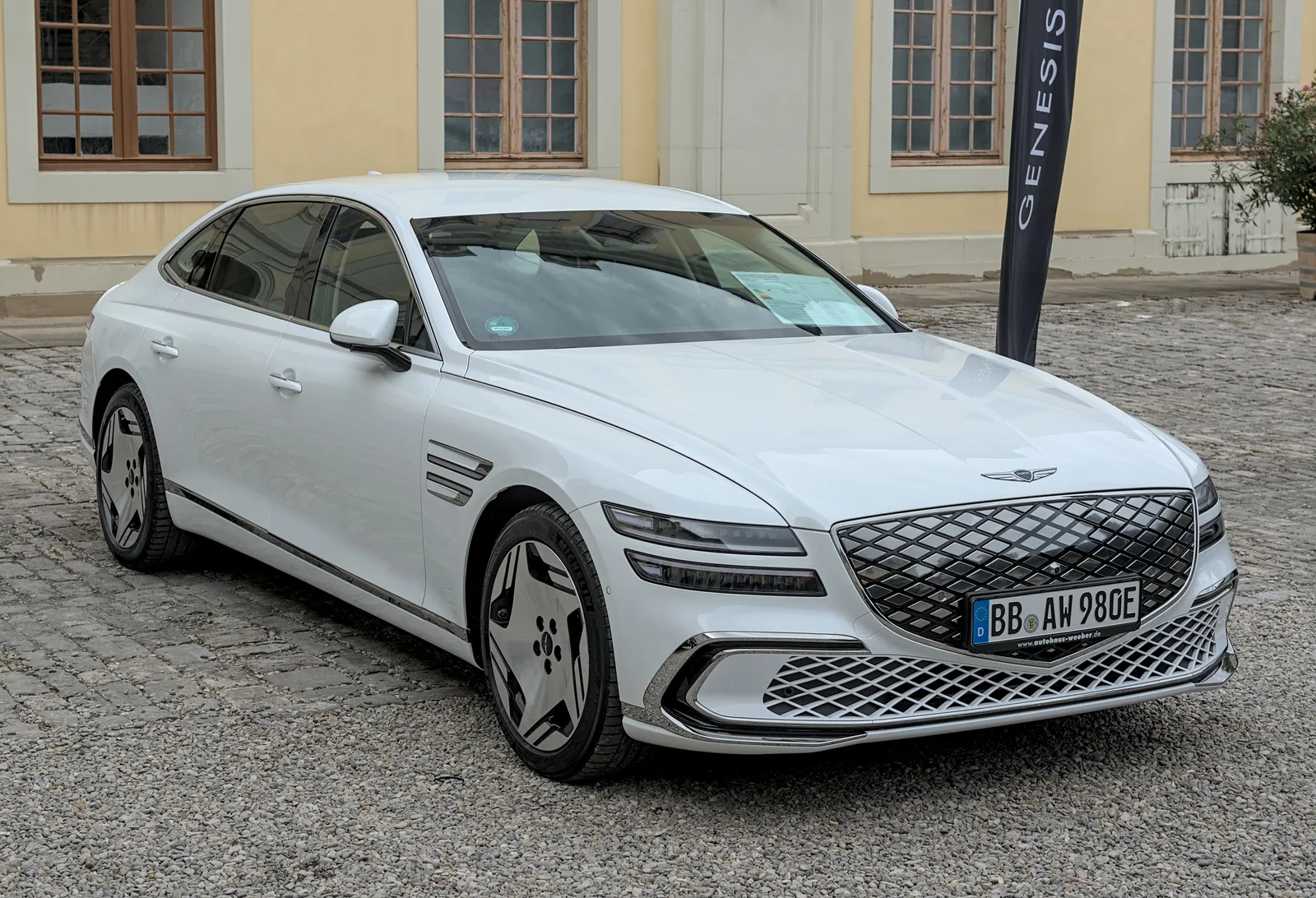 Genesis Electrified G80 2026 vue 3/4 avant berline blanche extérieur cour pavée