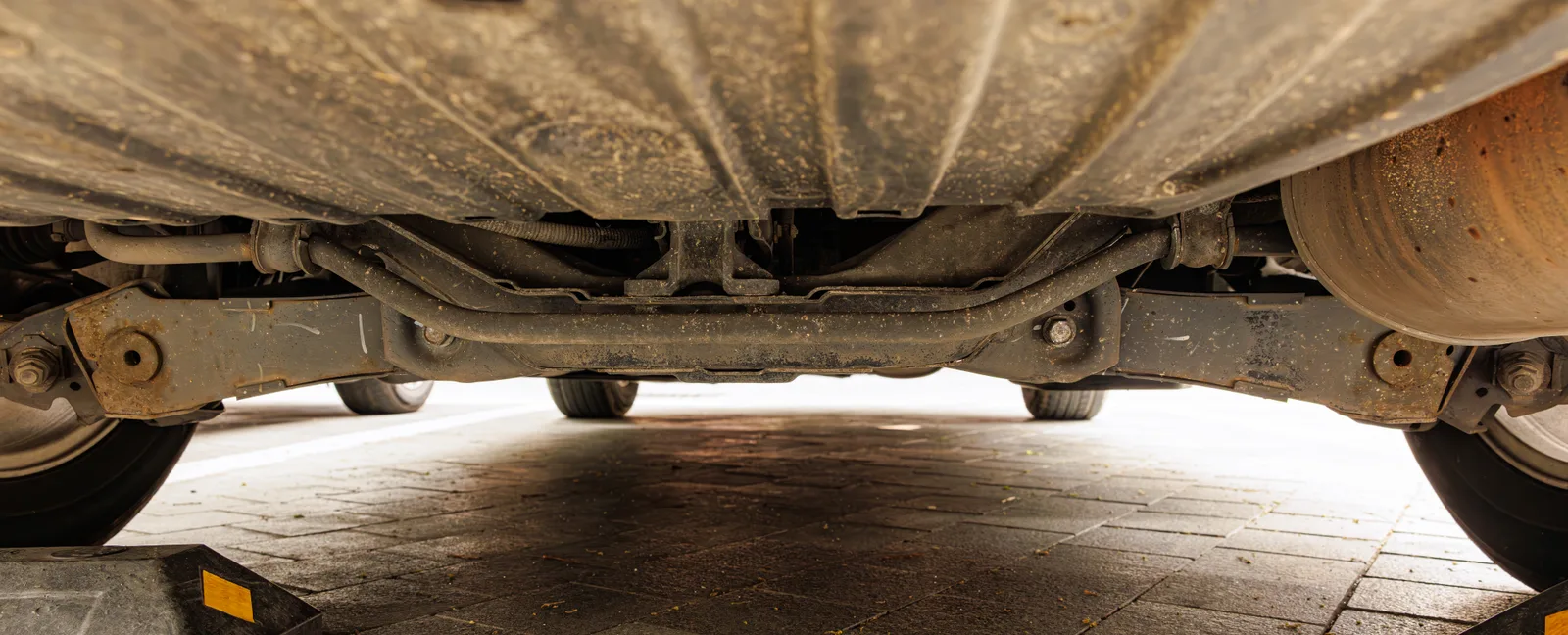 Train arrière d'un véhicule vu de dessous sur un pont élévateur — bras de suspension, silentblocs et points de réglage visibles