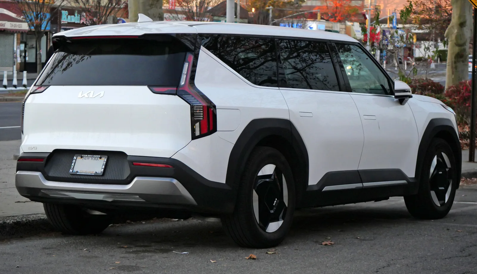 Kia EV9 2026 vue 3/4 arrière SUV électrique blanc sur route urbaine