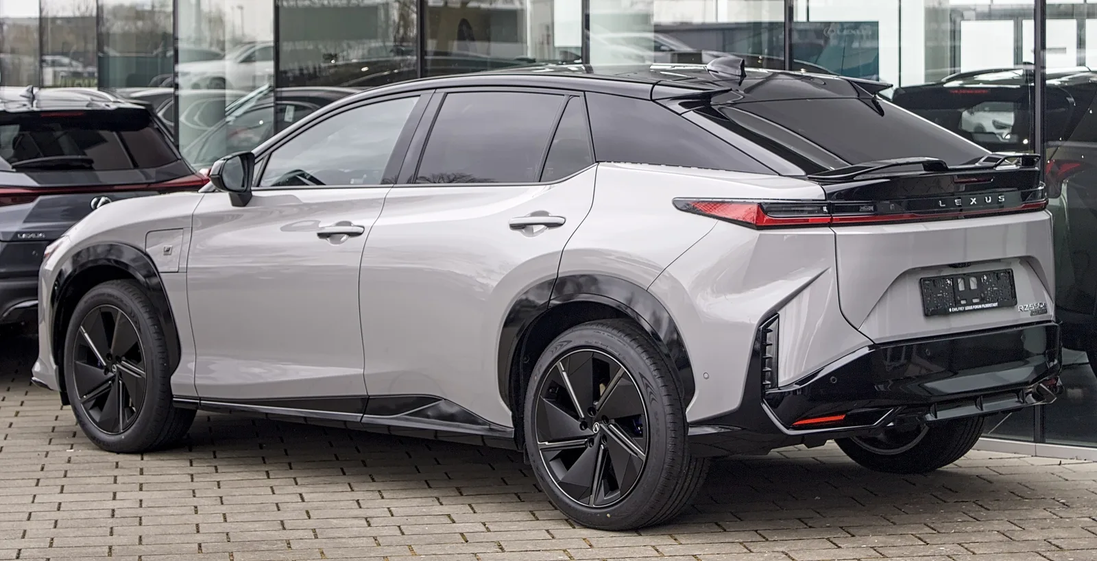 Lexus RZ 550e F Sport gris et noir vu de trois quarts arrière devant une concession, bandeau lumineux et becquet arrière