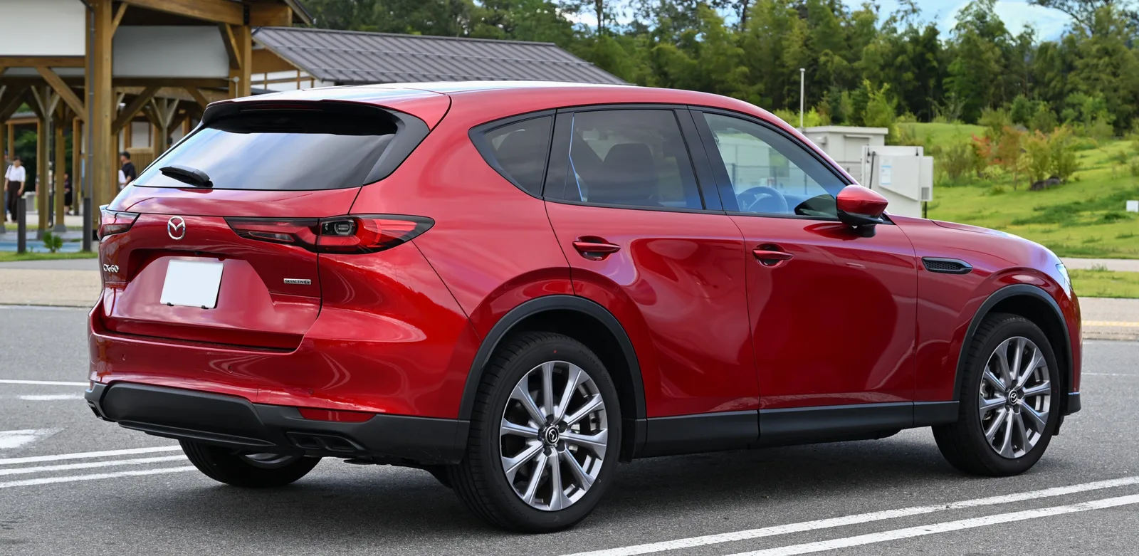 Mazda CX-60 2026 vue arrière trois quarts SUV rouge sur parking devant paysage boisé