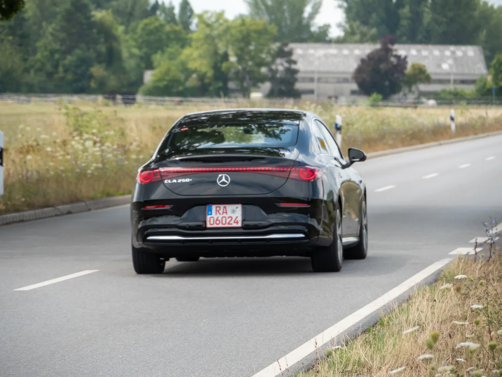 Mercedes CLA 250+ électrique noire vue de l'arrière sur une route de campagne, berline qui récupère 325 km en 10 minutes selon Mercedes