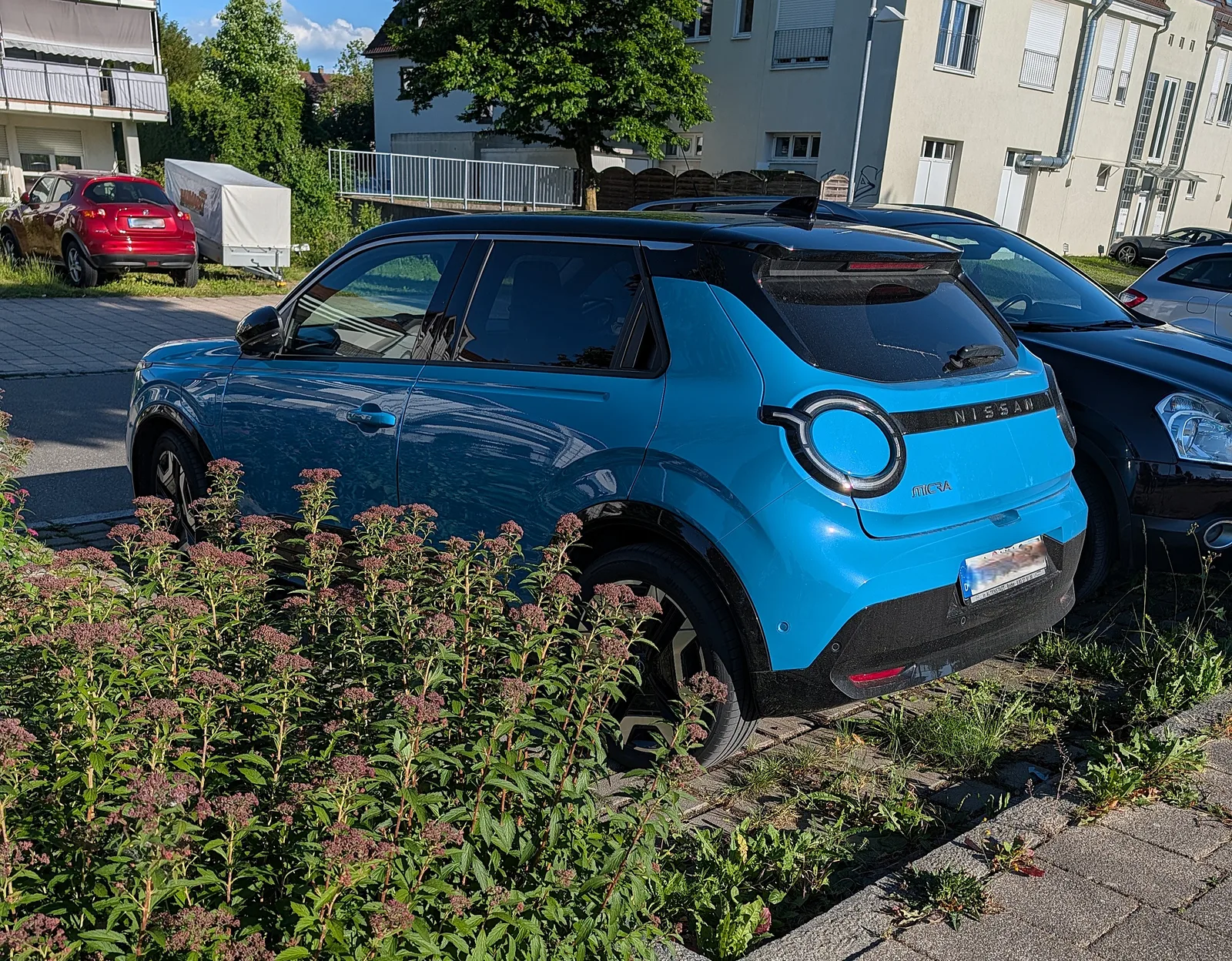 Nissan Micra électrique 2026 vue 3/4 arrière citadine bleue garée dans une rue résidentielle
