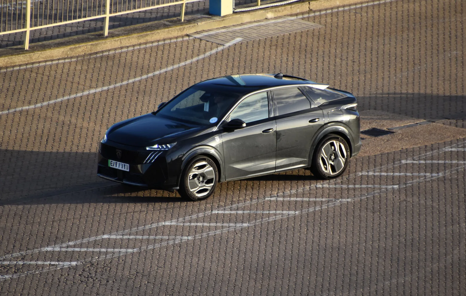 Peugeot e-3008 gris foncé vu de trois quarts avant sur un parking, SUV électrique assemblé à Sochaux