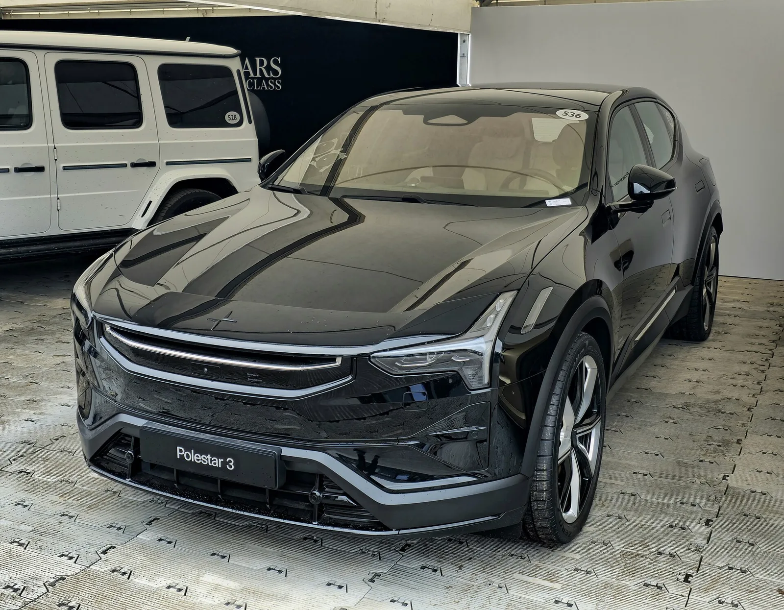 Polestar 3 noir vu de face sur un stand d'exposition, calandre fermée et optiques fines du SUV électrique