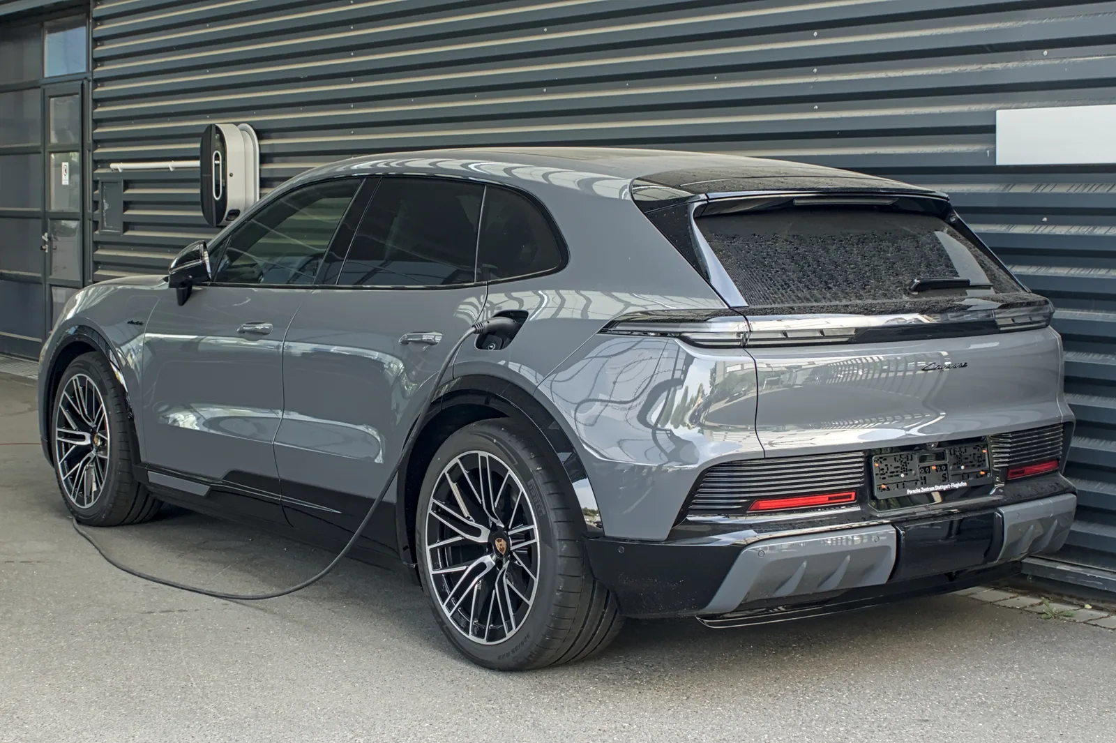 Porsche Cayenne Electric gris en charge sur une borne murale, vu de trois quarts arrière, SUV électrique capable de tracter 3 000 kg