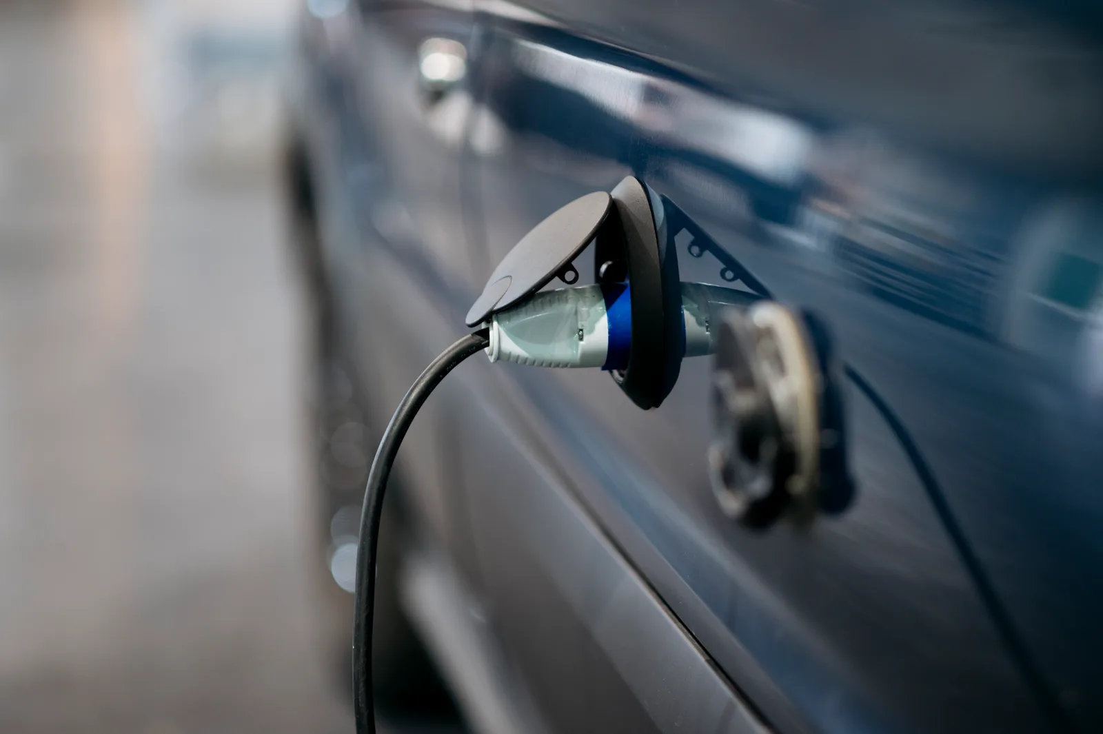 Voiture électrique grise en charge sur une borne publique en journée, câble branché dans une rue urbaine