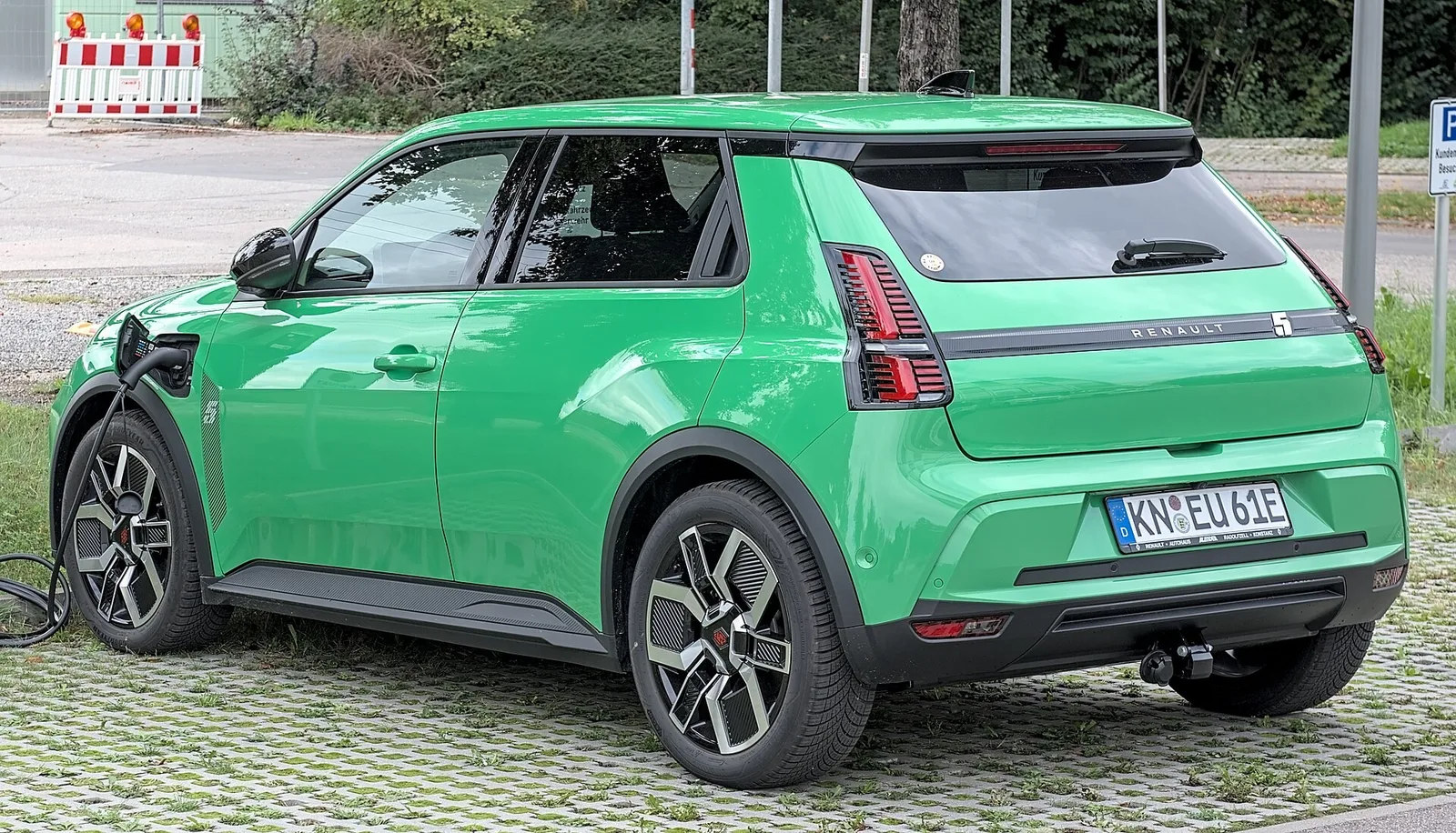 Renault 5 E-Tech électrique verte branchée sur une borne de recharge, vue de trois quarts arrière