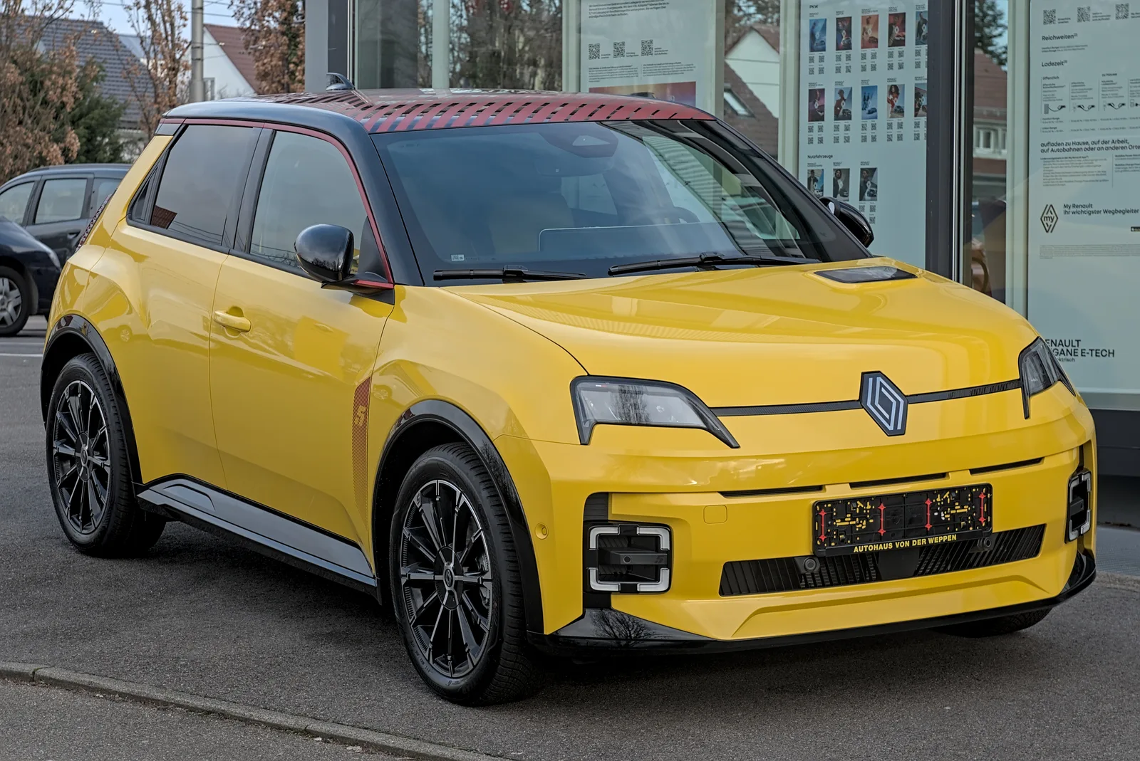 Renault 5 E-Tech Electric en jaune, vue 3/4 avant sur rue en ville, design signature visible avec DRL carrés et liseré rouge