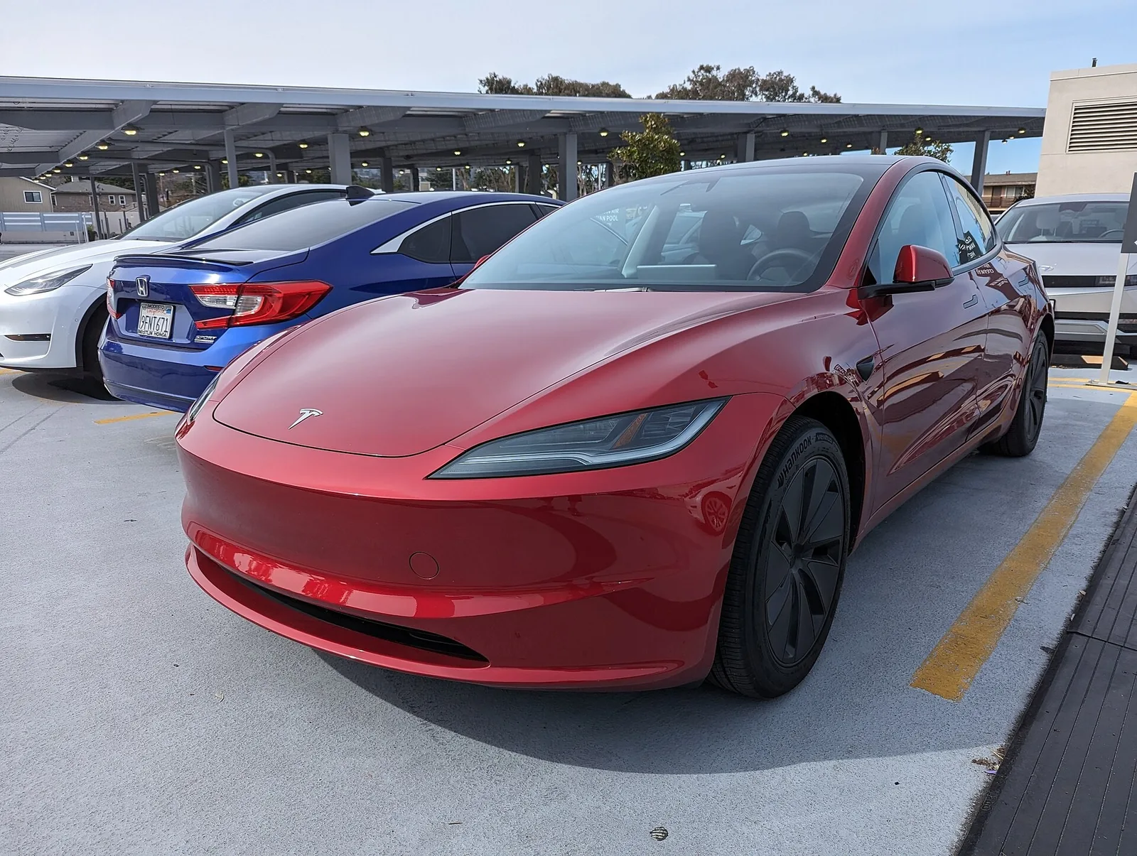 Tesla Model 3 Highland rouge garée sur un parking, berline électrique aux consommations autoroutières mesurées