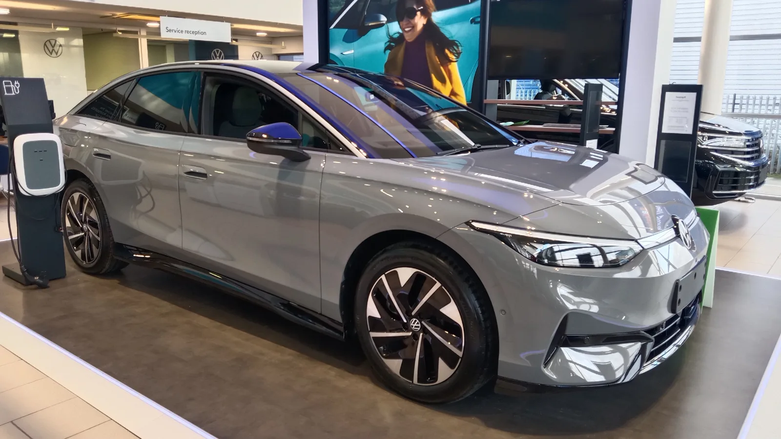 Volkswagen ID.7 Pro grise exposée en concession à côté d'une borne de recharge murale, berline électrique de 4,96 m