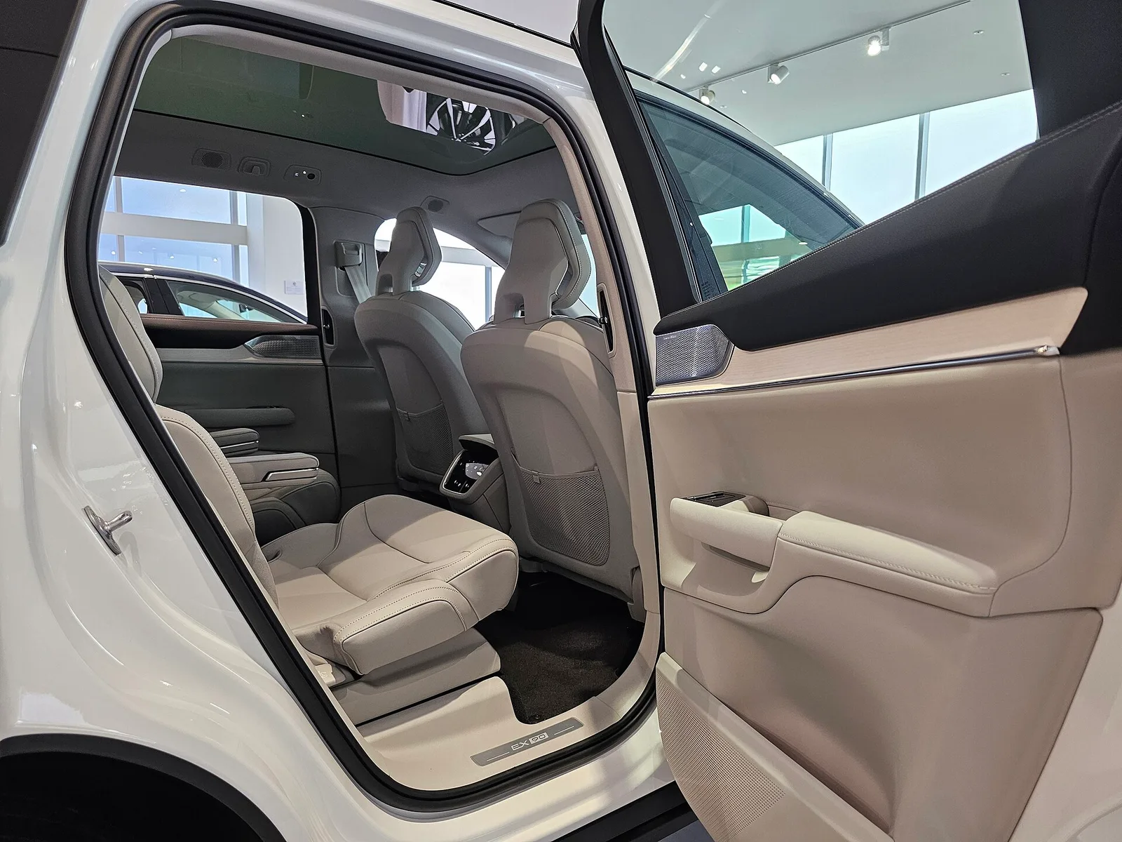 Sièges arrière en cuir clair du Volvo EX90 Ultra 2026 vus par la portière arrière ouverte, deuxième rangée du SUV électrique 7 places